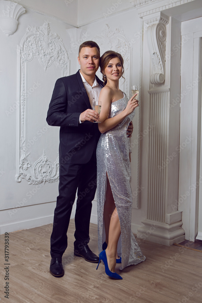 man in a black suit and a woman in a shiny dress stand with a glass of champagne