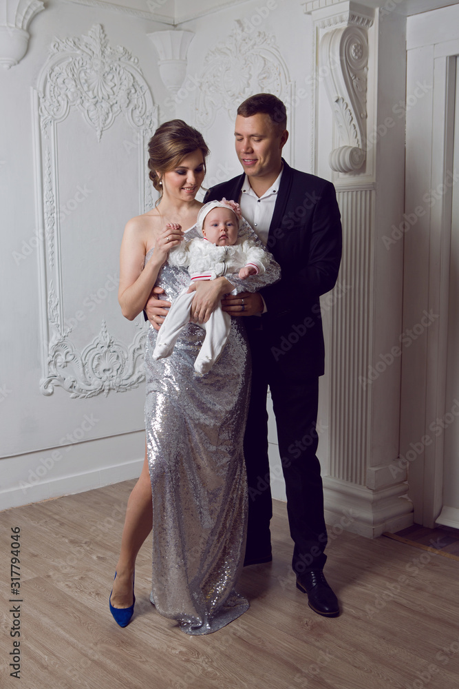 Fototapeta premium man in a black suit with a woman in a shiny long dress holding a little daughter
