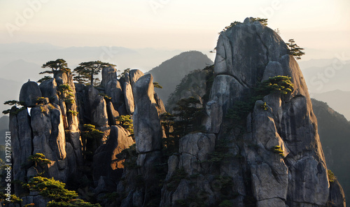 Huangshan Mountain in Anhui Province, China. View at sunrise from Dawn Pavilion viewpoint with a rocky outcrop and pine trees. Scenic view of peaks and trees with shadows on Huangshan Mountain, China. photo