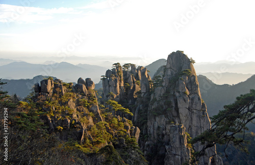 Huangshan Mountain in Anhui Province, China. View at sunrise from Dawn Pavilion viewpoint with a rocky outcrop and pine trees. Wide scenic view of peaks and trees on Huangshan Mountain, China. photo