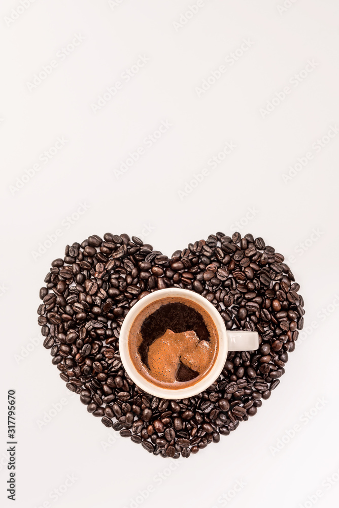 Fototapeta premium Top view of tasty coffee in cup or mug with heart made of coffee grains on white background