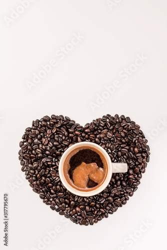 Top view of tasty coffee in cup or mug with heart made of coffee grains on white background