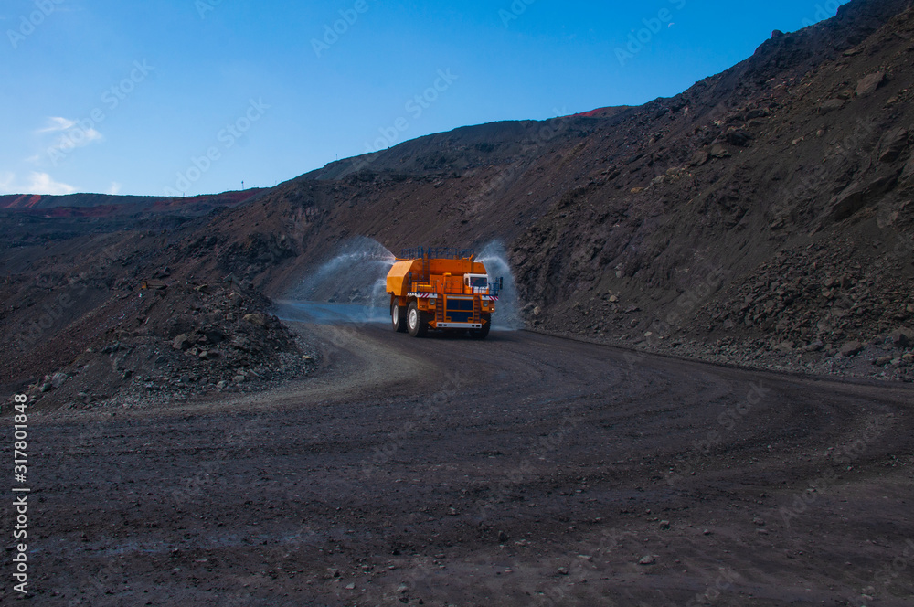 Heavy truck pours the road with water in the iron ore quarry. Dust removal, protection of the environment. Irrigation of the road from dust. The World’s Largest Sprinkler Truck Heavy truck pours the road with water in the iron ore quarry. Dust removal, protection of the environment. Irrigation of the road from dust. The World’s Largest Sprinkler Truck