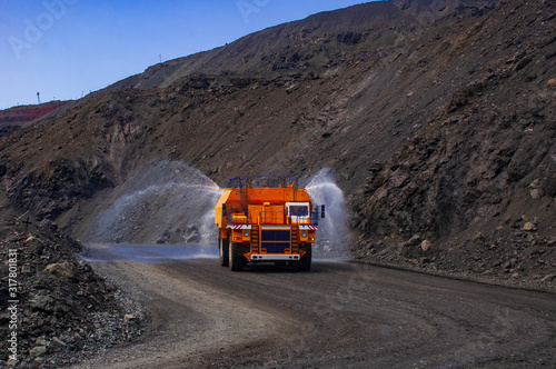 Heavy truck pours the road with water in the iron ore quarry. Dust removal, protection of the environment. Irrigation of the road from dust. The World’s Largest Sprinkler Truck