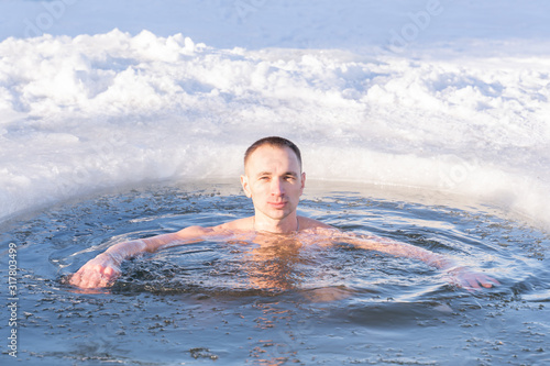 young man swims in an ice hole in cold water in winter, closeup