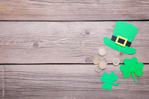 Happy Saint Patrick's of handmade paper clover leaves and hat with coins on grey wooden background.
