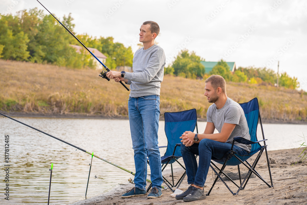 leisure and people concept. Happy friends with fishing rods on pier by lakeside. leisure and people concept. Happy friends with fishing rods on pier by lakeside.
