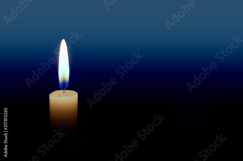 Close up of burning candle with bright yellow and blue flame against a blue gradient background