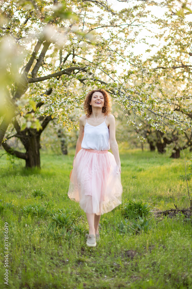 Young attractive woman with curly hair walking in a green flowered garden. Spring romantic mood Young attractive woman with curly hair walking in a green flowered garden. Spring romantic mood