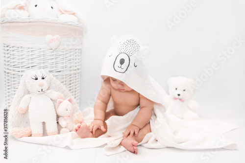 Cute baby under a white towel with a hood after a bath. The child sits in a towel with ears and looks down. Baby in towel isolated. Infant portrait. Health care concept.