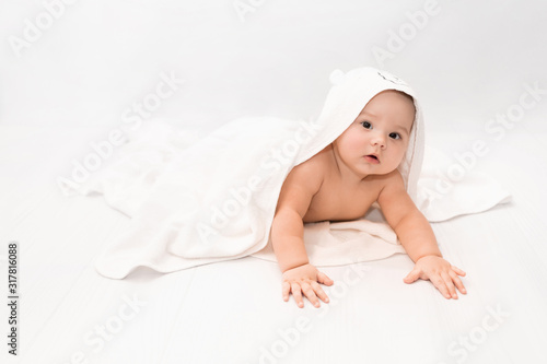 Cute baby under a white towel with a hood after a bath. Baby in a towel. Children's portrait. Healthcare concept.