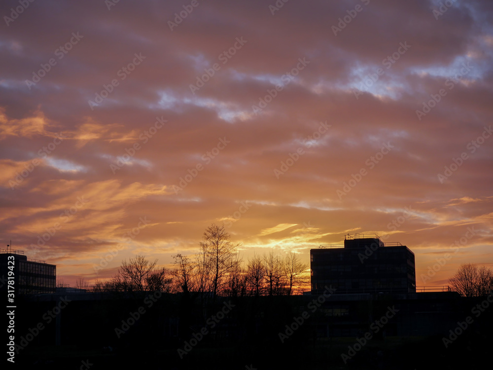 Silhouette of a building surrounded by trees at sunset, Warm glowing cloudy sky.