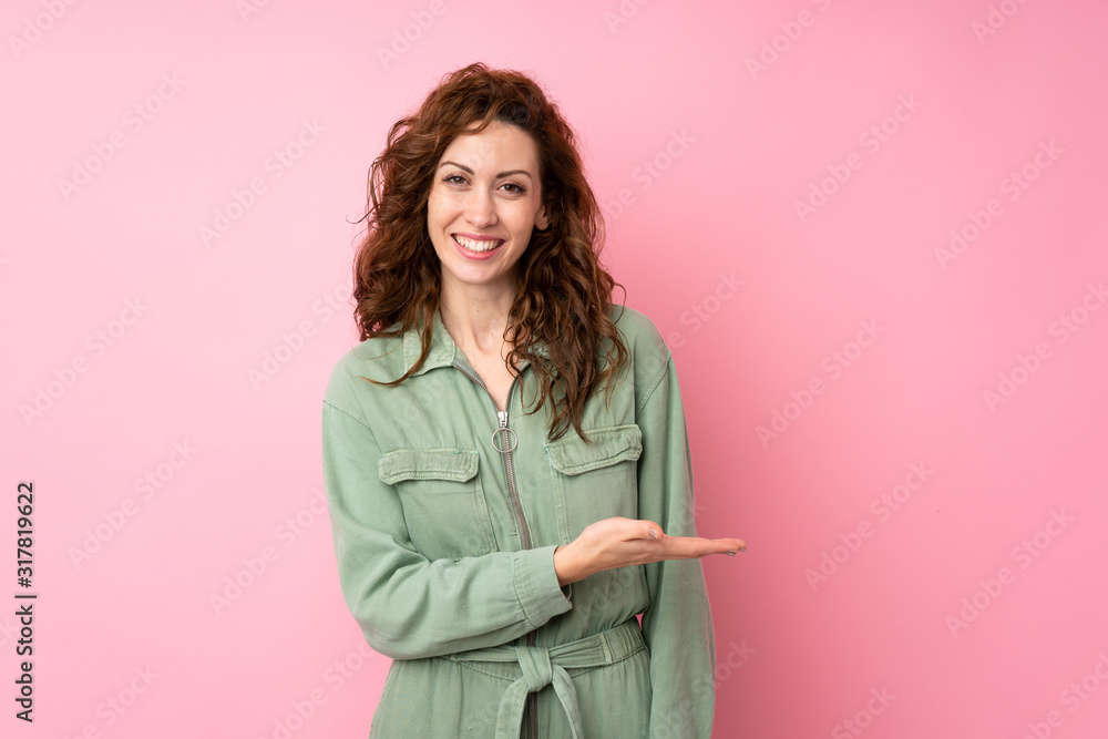 Young pretty woman over isolated pink background presenting an idea while looking smiling towards Young pretty woman over isolated pink background presenting an idea while looking smiling towards