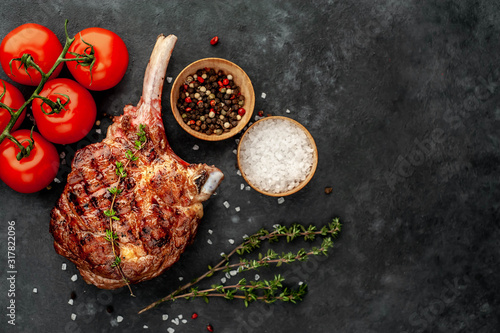Obraz na plátně grilled beef steak - tomahawk with spices, tomatoes, thyme on a stone background