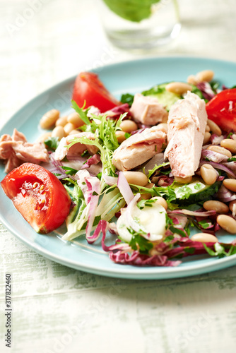 Healthy salad with tuna, cannellini bean, endive and tomatoes. Bright wwooden background. 
