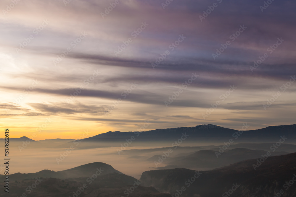 Vantage point view of valley and canyon filled with morning mist lighten by sunrise, vivid colors of the sky and distant impressive mountains