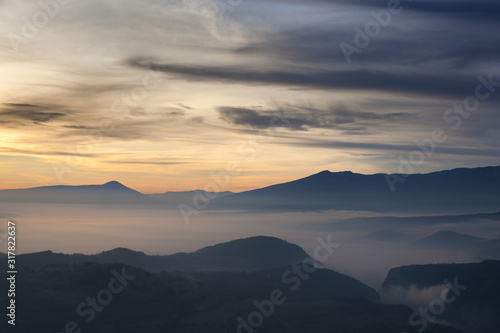 Vantage point view of valley and canyon filled with morning mist lighten by sunrise, vivid colors of the sky and distant impressive mountains © Nikola