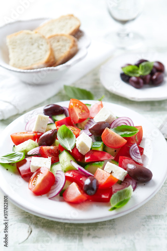 Healthy and tasty salad with feta cheese, kalamata olives, cherry tomatoes and fresh basil. Bright wooden background. 
