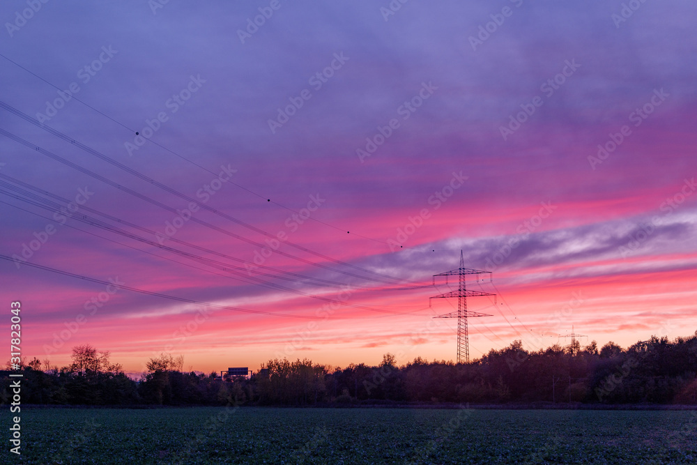 Beautiful dramatic purple and pink cloud and sky after storm and raining over agricultural field and high voltage tower on countryside in Germany. Nimbostratus cloud during sunset. 