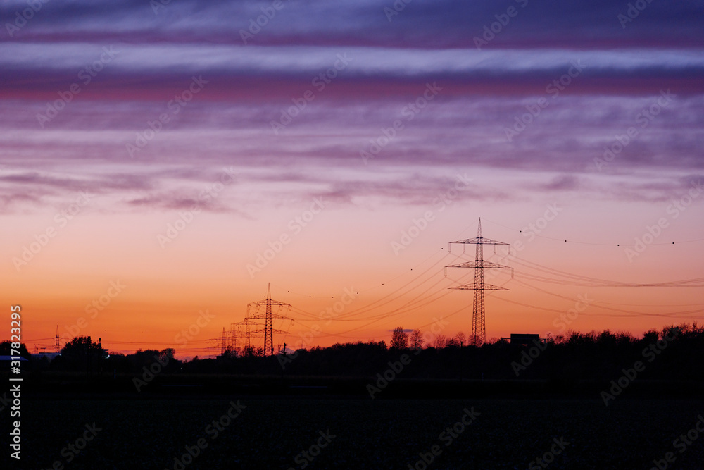 Naklejka premium Beautiful dramatic orange and blue cloud and sky after storm and raining over agricultural field and high voltage tower on countryside in Germany. Nimbostratus cloud during sunset.