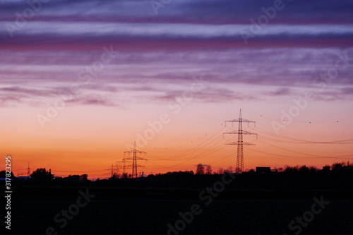 Beautiful dramatic orange and blue cloud and sky after storm and raining over agricultural field and high voltage tower on countryside in Germany. Nimbostratus cloud during sunset. 