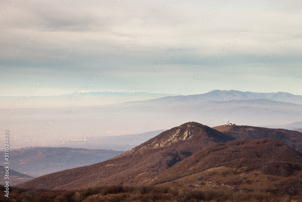 Distant city of Nis, Serbia, from a viewpoint on Svrljig mountains, radio tower at the top of the hill and cloudy sky Distant city of Nis, Serbia, from a viewpoint on Svrljig mountains, radio tower at the top of the hill and cloudy sky