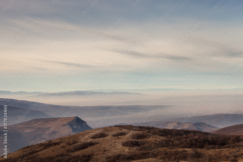 Distant, mist covered city of Nis in Serbia, cloudy sky, foreground sinkholes on the mountain and horizon Prokletije mountain covered by snow