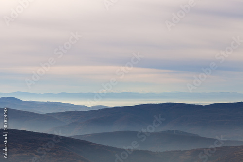 Distant Prokletije mountains covered by snow and foreground mountain layers on a misty, foggy morning and colorful sky
