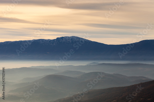 Blue hour view of Trem summit on Dry mountain (Suva planina), colorful sunrise sky and layers of mist in above the hills below