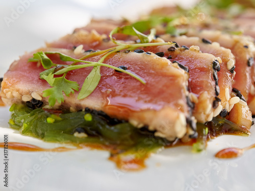 Seared ahi tuna slices on a bed of seaweed salad sprinkled with sesame seeds and oil and garnished with sprouts