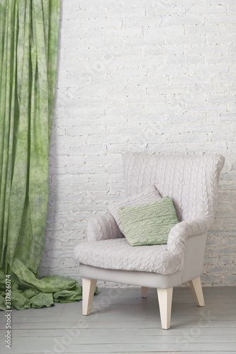 soft armchair near white brick wall with green curtain. Arm-chair with knit upholstery
