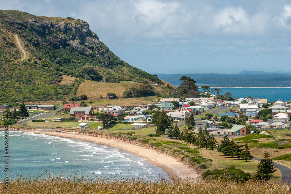 Stanley, Tasmania, Australia - December 15, 2009: The town at the base of The Nut volcanic plug. Beach and surf. Cloudscape and blue ocean with mountains in back.