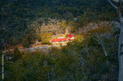 A valley between mountains and hills. The house on the road lit by the sun, surrounding forest in the dark. Yarrangobilly Caves, Kosciuszko National Park, NSW, Australia. photo