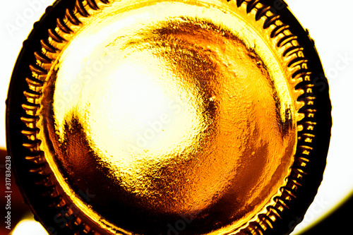 Glass lemonade bottle with contour lighting. Bottom of a glass beer bottle close-up, background. Screensaver with the bottom of a ale bottle. Abstract surface made of brown plastic with orange light.  photo