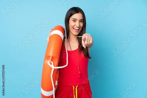 Lifeguard woman over isolated blue background with lifeguard equipment and points finger at you