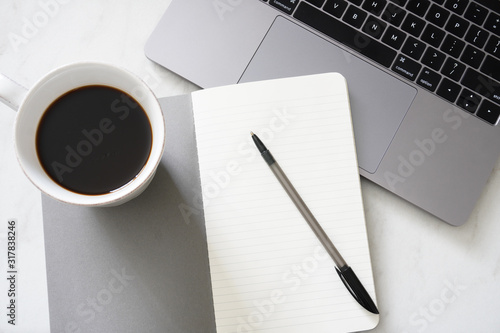 An open notebook and pen ready to write a to do list with a cup of coffee and laptop on a desk; minimal clean gray and white; flat lay
