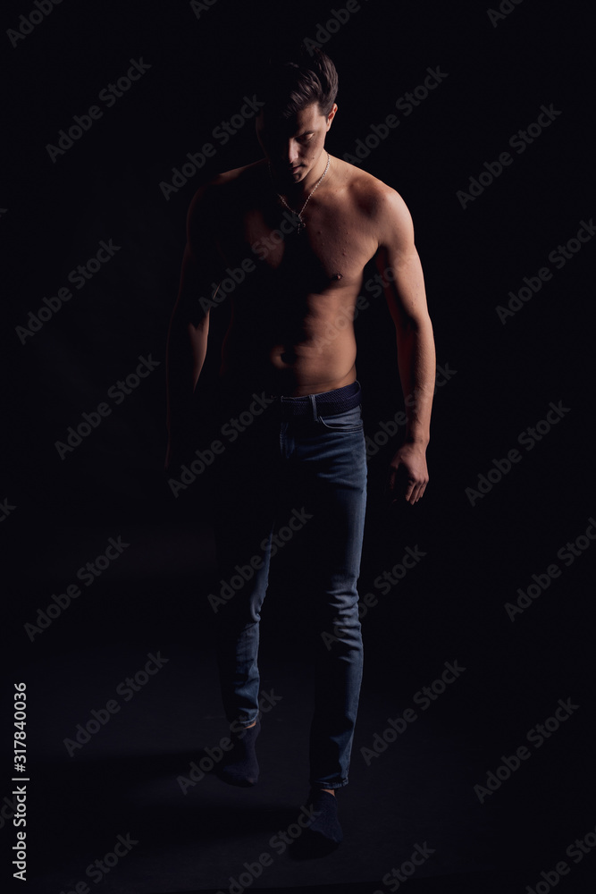 barechested guy with a dramatic light in the Studio on a black background. lowered his head barechested guy with a dramatic light in the Studio on a black background. lowered his head