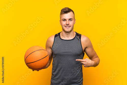 Young handsome blonde man holding a basket ball over isolated yellow background with surprise facial expression