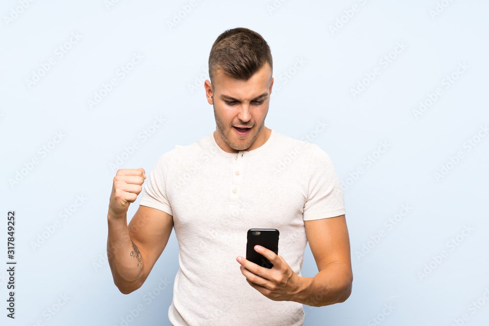 Young handsome blonde man over isolated blue background using mobile phone Young handsome blonde man over isolated blue background using mobile phone