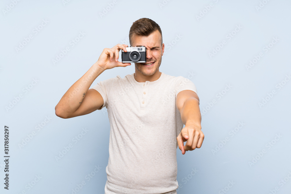 Young handsome blonde man over isolated blue background holding a camera Young handsome blonde man over isolated blue background holding a camera