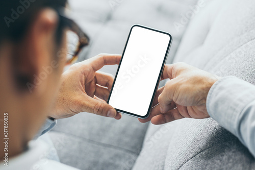 Mockup image blank white screen cell phone.men hand holding texting using mobile on sofa at home office.background empty space for advertise text.people contact marketing business and technology