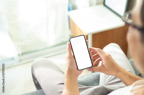 Mockup image blank white screen cell phone.men hand holding texting using mobile on sofa at home office.background empty space for advertise text.people contact marketing business and technology