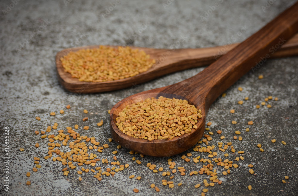 Fenugreek seeds in wooden spoon on textured background Fenugreek seeds in wooden spoon on textured background