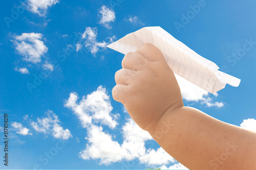 boy's hand holding a white paper rocket with a bright blue background.
