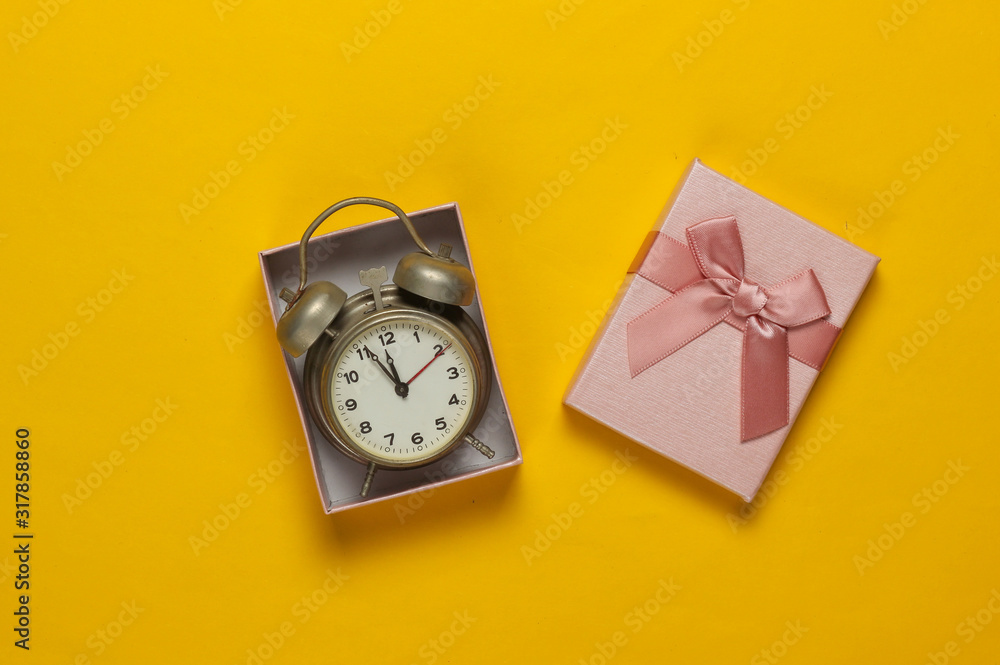 Retro alarm clock in gift box with bow on yellow background. 11:55 am. New Year, Christmas.concept. Top view Retro alarm clock in gift box with bow on yellow background. 11:55 am. New Year, Christmas.concept. Top view