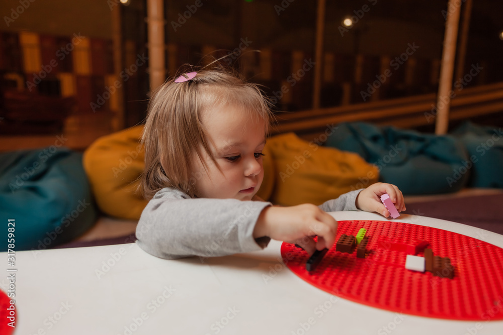 Naklejka premium Little girl plays toy bricks at table in children's entertainment center