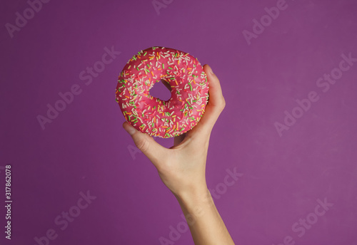 Female hand holds a glazed donut on purple background. Sweet dessert. Top view.