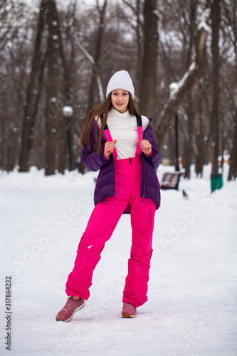 Portrait of a young beautiful woman in a ski suit posing in winter park