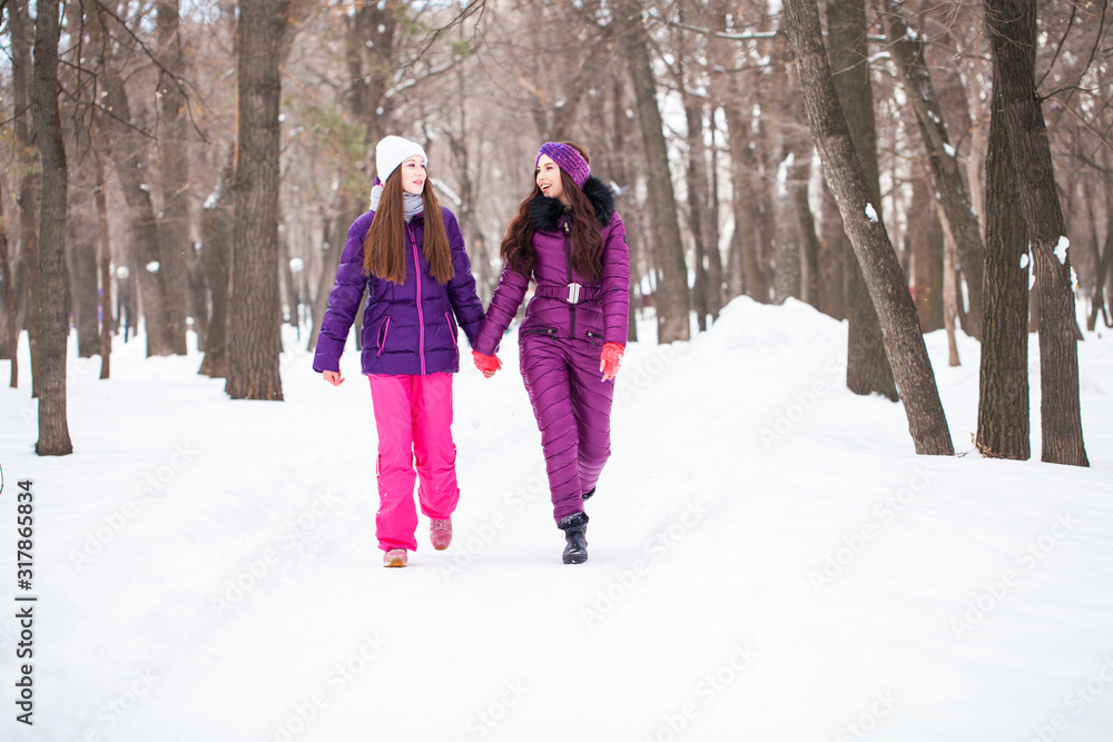 Two happy beautiful girlfriends walk in the winter in a city park