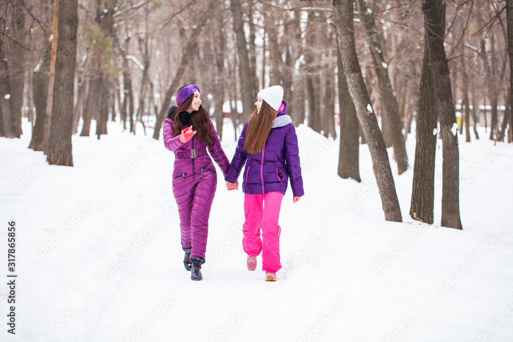 Two happy beautiful girlfriends walk in the winter in a city park